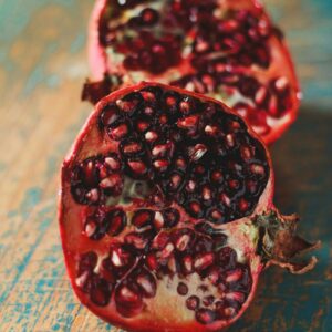 A fresh pomegranate cut in half, showcasing its vibrant seeds on a rustic wooden surface.
