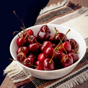 A white bowl filled with fresh, ripe cherries on a wooden table, perfect for healthy snacking.
