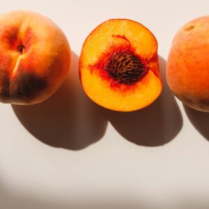 Bright and vibrant peaches with a sliced half showcasing their juicy texture, casting shadows.