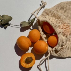 Close-up of apricots spilling from a string bag on a sunlit surface.