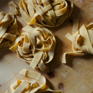 Close-up of freshly made tagliatelle pasta nests on a rustic wooden board, capturing the essence of traditional Italian cuisine.