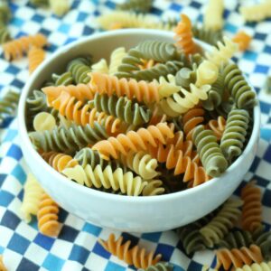 Close-up of uncooked tricolor fusilli pasta in a white bowl with a blurred background.