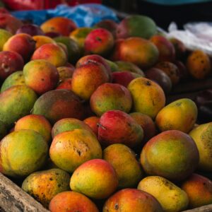 Colorful mangoes in a rustic wooden crate at a bustling market, showcasing fresh produce.