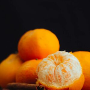 Vibrant image of peeled orange with whole oranges and cinnamon sticks on a wooden board.
