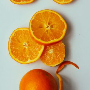 Vibrant orange slices and a whole orange with peel on a white surface, showcasing freshness.